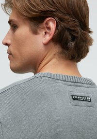 Grauer Strickpullover mit einem gerippten Kragen, der hinten ein schwarzes Etikett mit der Aufschrift "POLAR EXP." und "CAMP DAVID" trägt.