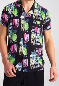 Camisa de manga corta hecha de tela ligera, con fondo negro y estampados tropicales coloridos en rosa, verde y azul.