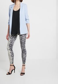 Blazer azzurro sopra una canotta nera, abbinato a leggings a stampa serpente bianca e nera e tacchi neri con cinturini. Tessuti lisci, stile aderente.