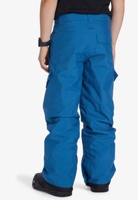 Blå snöbyxor gjorda av slitstarkt material, med en lös passform, justerbart midjeband, flera fickor och förstärkta mudd.