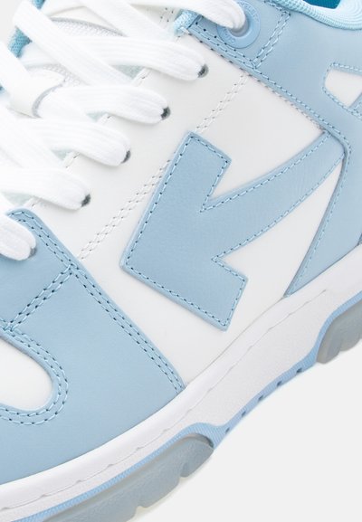 Κοντινή λήψη λευκού και ανοιχτό μπλε αθλητικού παπουτσιού που δείχνει τα κορδόνια, τις ραφές και το σχέδιο σε σχήμα βέλους στο πλάι.