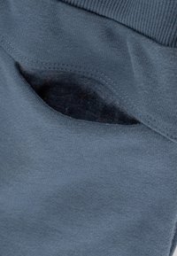 Blauer Baumwollstoff mit einer sichtbaren Taschenöffnung, ausgestattet mit einer sanften Textur. Die Naht um die Tasche ist ordentlich verarbeitet.