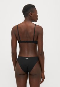 Ensemble de bikini noir avec des bretelles ajustables et un dos à agrafe. Le bas a un design taille basse avec un petit logo Nike blanc à l'arrière.