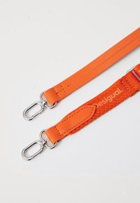 Pomarańczowe paski wykonane z gładkiego materiału syntetycznego i tkanej nylonowej, z metalowymi srebrnymi klamrami do mocowania, z oznaczeniem marki na jednym pasku.