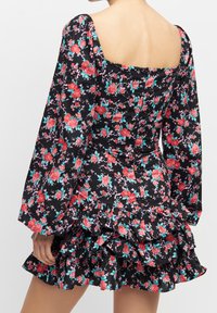 Černé květinové šaty s volánkovým lemem, zdobené červenými a tyrkysovými květy, čtvercovým výstřihem a dlouhými nafouknutými rukávy. Tkanina vypadá lehce.