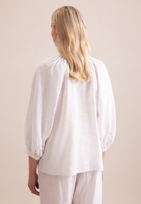 Blusa bianca in lino con scollatura arricciata, maniche a baloon e dettagli ai polsini. Tessuto morbido e leggero con una vestibilità rilassata.