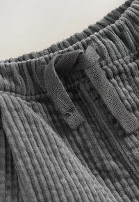 Șorturi gri din corduroy cu o suprafață texturată, cu nervuri. Prezintă un talie elastică și un șnur legat pentru ajustare.