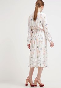 Vestido midi floral de tela blanca ligera, con patrones en rosa, azul y verde, cintura fruncida, acentos de encaje y dobladillo con volantes.