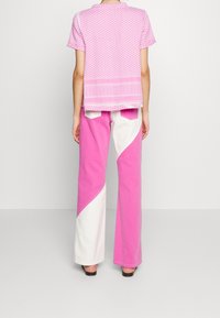 Top corto de manga corta con un patrón en rosa y un escote redondo, combinado con pantalones de pierna ancha que tienen un diseño a bloques de color en rosa y blanco.