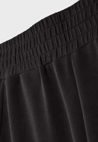 Gros plan sur un tissu noir avec une ceinture élastique présentant plusieurs rangées de couture et un matériau froncé en dessous.
