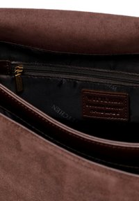 Wnętrze brązowej torebki z zamszu z kieszonką na zamek i skórzaną metką z wytłoczonym tekstem. Gładka podszewka z delikatnym połyskiem.