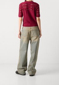 Burgundy neulepaita, jossa on leikattuja pyöreitä kuvioita ja ribbidesign, yhdistettynä vaaleisiin leveälahkeisiin farkkuihin, joissa on rento malli ja läpivienneet taskut.