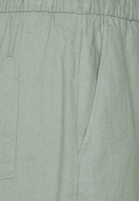 Light green linen fabric with a textured finish. Features an elastic waistband and a side pocket, highlighting casual design aspects.