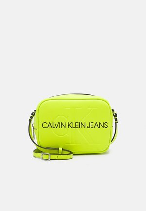 Kleine rechteckige hellgelb-grüne Umhängetasche mit schwarzem "Calvin Klein Jeans" Text und verstellbarem Riemen.