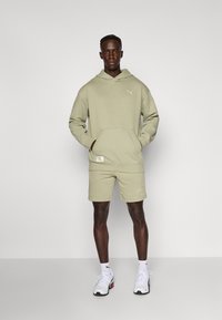 Lichtgroene hoodie met een kangoeroezak en geribbelde boorden, gecombineerd met bijpassende shorts. Witte sneakers met zwarte accenten maken de outfit compleet.