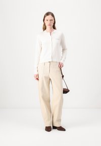 Lys beige strikket cardigan med rund hals og subtil brodering, sammen med høytlivde, vide beige bukser og brune støvler.