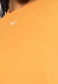 En person som bär en orange Nike-t-shirt med en vit Nike-swoosh-logotyp nära halsringningen, som visar axel- och nackområdet.