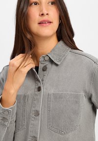 Szara kurtka dżinsowa z zapięciem na guziki, dwoma kieszeniami na piersi, zatrzaskami oraz usztywnionym kołnierzem o miękkiej teksturze.