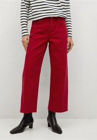 Pantalones anchos rojos de algodón, con dobladillo sin acabar y bolsillos delanteros, combinados con una blusa de rayas en blanco y negro y botines negros.