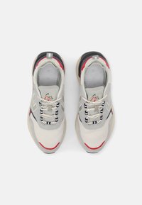 Ljusgrå sneakers med nätmaterial, vadderad krage, röda och blå accenter samt ett mönstrat sål. Har snören och logotyp på tungan.