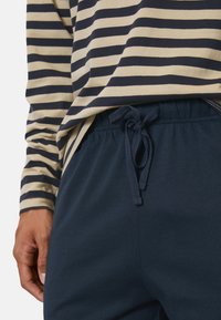 Chemise à manches longues rayée en beige et bleu marine, assortie à un pantalon bleu marine à cordon de serrage avec une texture douce et une taille élastique.