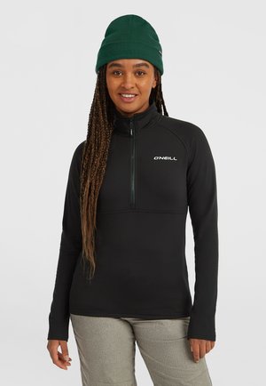 Zwarte fleece zip-up top met opstaande kraag, voorzien van een gedeeltelijke ritssluiting en een logo op de borst. Draag het met grijs gestructureerde broek en een groene beanie.