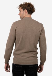 Jersey marrón texturizado con mangas largas y cuello redondo, con puños y dobladillo acanalados, combinado con pantalones vaqueros oscuros.