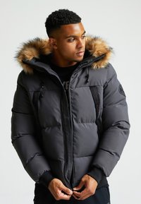 Tumesinine puhvjak Siga, millel on karusnaha voodriga kapuuts, tõmblukuga esiosa ja mustad detailid. Omab elastseid mansette ja küljetaskuid.