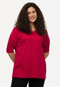 V-hals, langarm shirt in felrood katoen met plooidetails bij de mouwen. Ontspannen pasvorm en een gladde textuur.