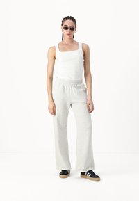 Lette grå joggebukser med elastisk midje, kombinert med en tettsittende hvit tank topp og svarte sneakers med hvite striper.
