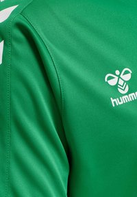 Zielony sportowy trykot z białym logo hummel na piersi i białymi szewronami na szwie barkowym.