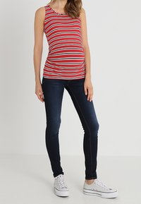 Top sin mangas a rayas rojas y blancas, hecho de tela de canalé, combinado con jeans ajustados azul oscuro y zapatillas blancas.