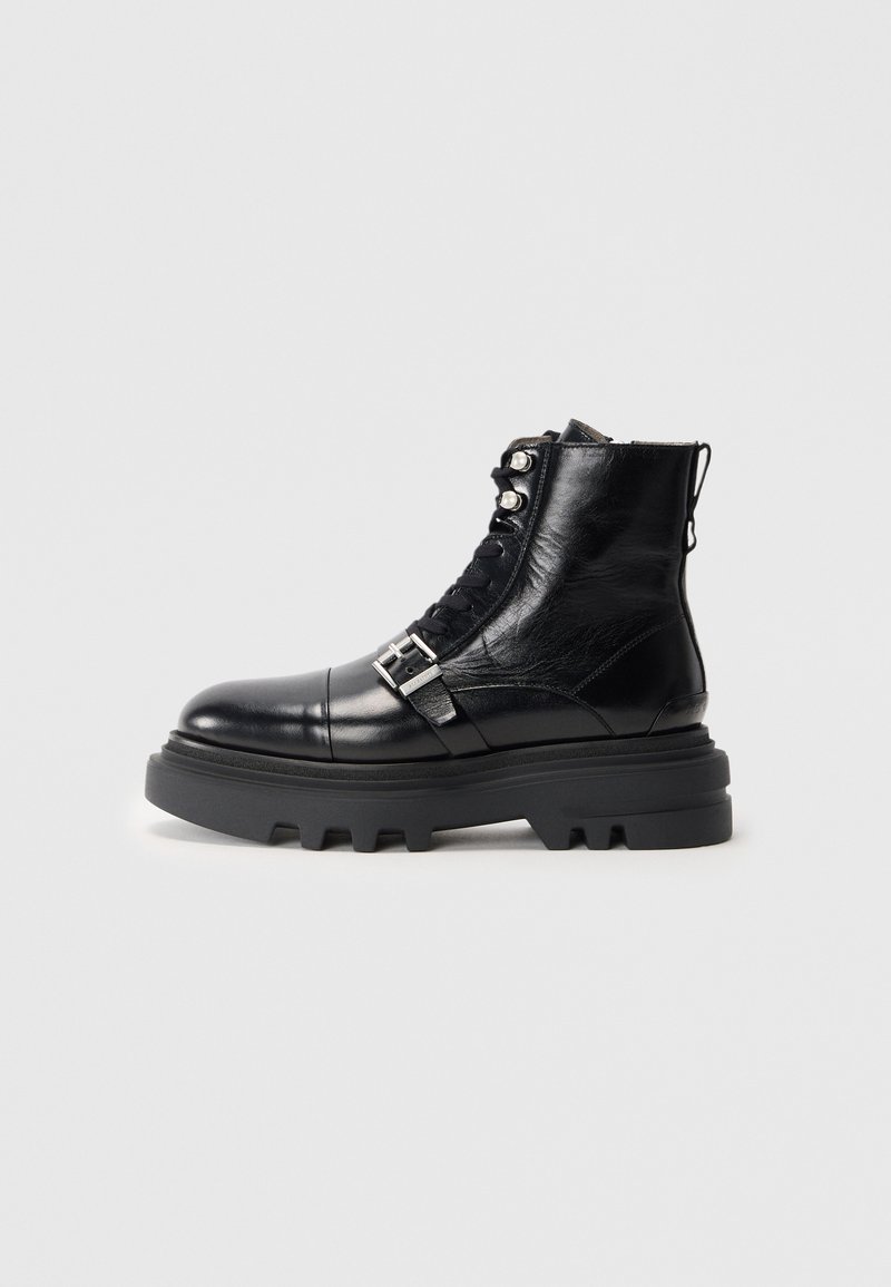 Black leather ankle boot with textured finish, featuring lace-up design, metal hardware accents, and thick rubber sole with pronounced tread.