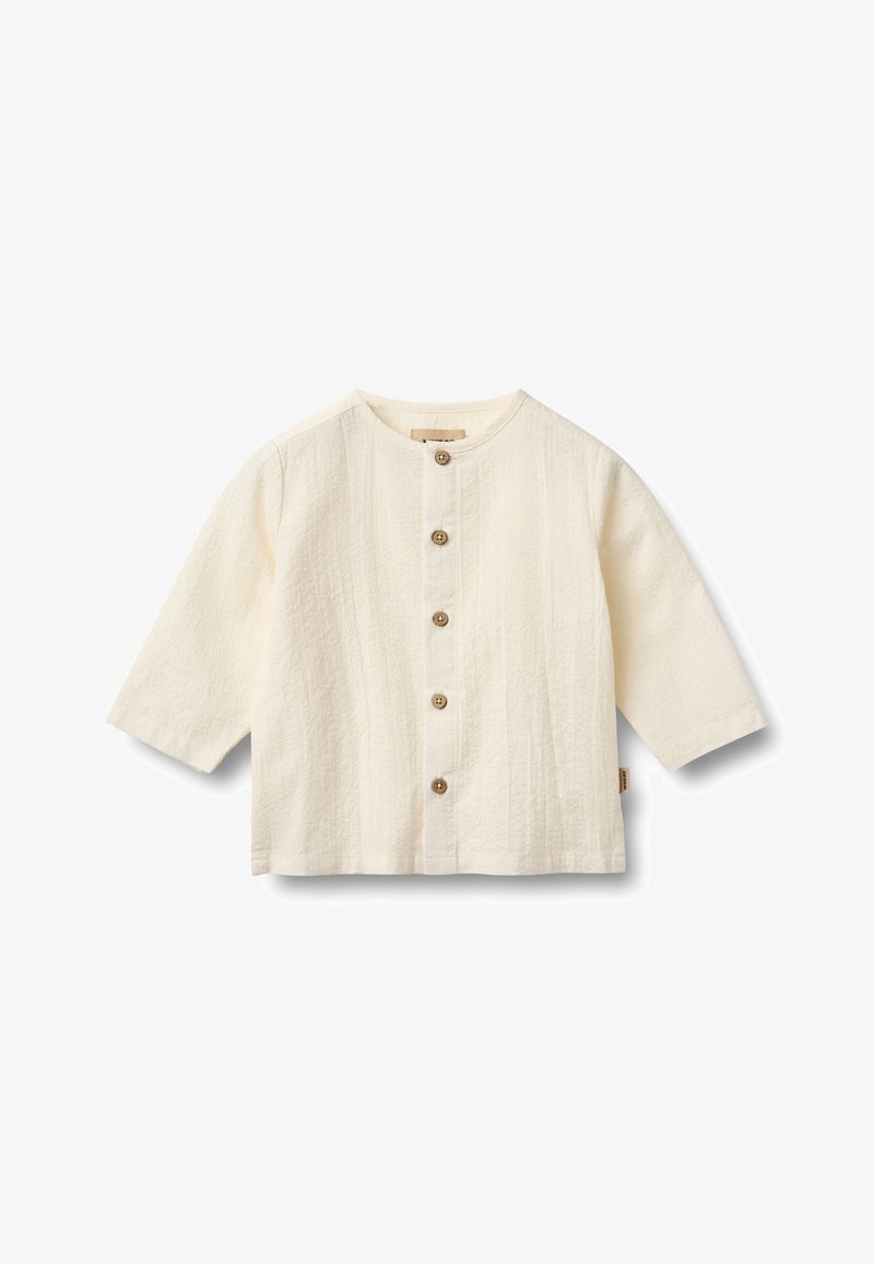 Chemise blanche texturée avec un col rond et des manches trois-quarts. Dotée de boutons marron sur le devant et d'une étiquette en tissu sur le côté.