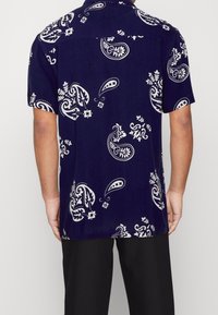 Krátký rukáv námořnicky modrá košile na knoflíky s bílým vzorem paisley, s límečkem a volnějším střihem. Hladká látka s mírným leskem.