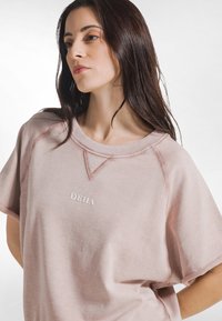 Felpa a maniche corte rosa chiaro in tessuto morbido, con scollo arrotondato e ricamo "DEHA" sul davanti con cuciture a contrasto.