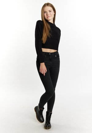 Mustat lyhyet neuleet, joissa on ribbikuvio, yhdistetty mustiin kapeisiin farkkuihin. Mallilla on jalassa mustat nauhaketjut, joissa on paksu pohja.
