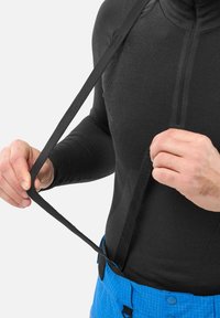 Schwarz sitzendes Baselayer aus strukturiertem Gewebe, mit hohem Kragen und verstellbaren schwarzen Trägern, kombiniert mit blauen Hosen im karierten Muster.