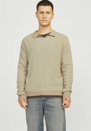 Pull en tricot beige avec un col polo, tissu texturé, manches longues et ourlet côtelé, porté sur une couche intérieure marron.