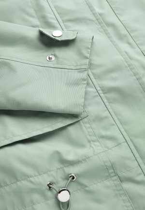 Manche de veste vert clair avec poignet à bouton-pression et ourlet ajustable à cordon avec embouts métalliques et coutures cousues.