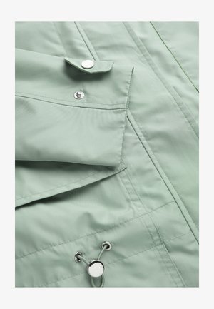 Lysegrøn jakkeærme med trykknapmanchet og justerbar snørre med metalstopper samt syninger.