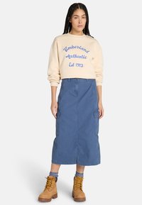 Beige collegepaita sinisellä tekstillä, yhdistetty knee-length sinisiin hameisiin, joissa on cargo-taskut ja vaaleat nauhaketjut kengät.