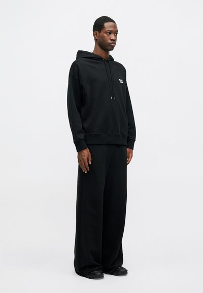 Set de hanorac și pantaloni sport negri, confecționat din bumbac moale. Hanoracul are un șnur de ajustare și un logo mic, având o croială lejeră și picioare largi.