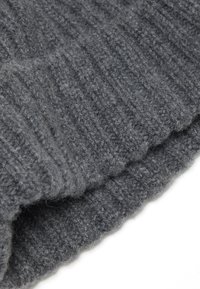 Primer plano de tejido de lana gris oscuro tricotado plegado con textura acanalada sobre un fondo blanco.