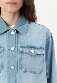Lyseblå denimjakke med sølvfargede nagler, klassisk krage, frontlommer og trykknappelukking.