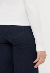 T-shirt branco de manga longa com texturas em relevo, combinado com jeans de ganga escura de cintura alta que apresentam bolsos traseiros e um acabamento suave.