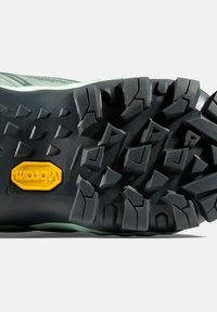 Sula av svart gummi med djupa spår, med en gul Vibram-logotyp. Överdel i ljusgrön, strukturerad för bättre grepp och stöd.