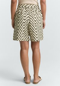 Shorts arrivés au genou en crème avec des rayures en zigzag noires. Présentent une taille froncée et deux poches arrière. Tissu léger avec une texture lisse.
