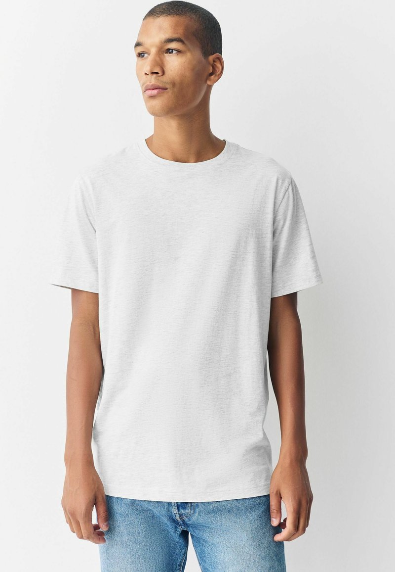 Kortärmad t-shirt i ljusgrått bomull. Rund halsringning, avslappnad passform, slät textur, inga synliga mönster eller varumärken. Bärs med blå jeans.