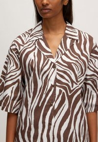 Braun-weißes Kurzarmhemd mit einem Zebra-Streifen-Muster, ausgestattet mit einem Kragen und einer Knopfleiste. Glatte Stofftextur.